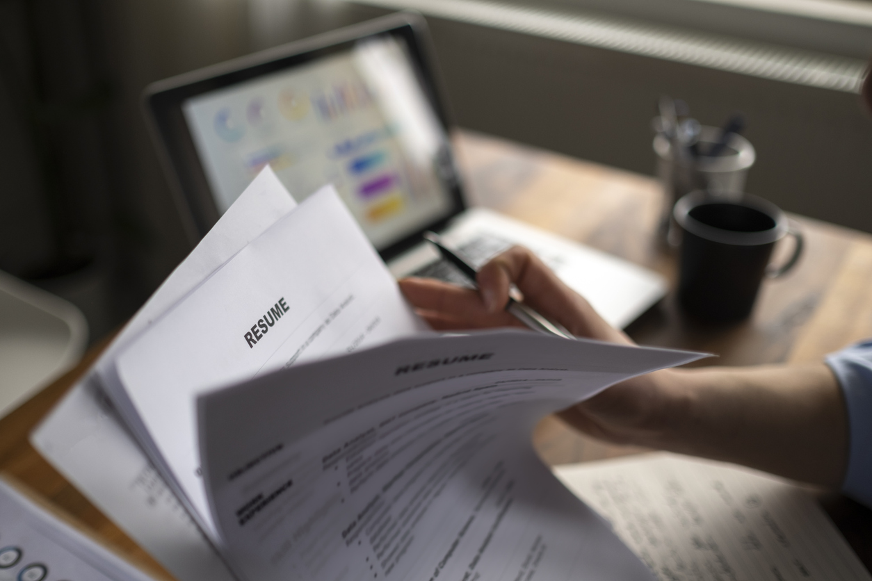 A hiring manager at an office desk reviewing printed resumes and a cover letter with a pen in hand, focused expression, daytime office setting