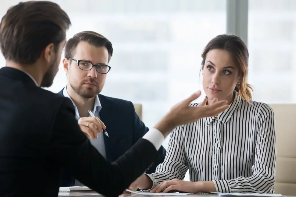 A job candidate speaking thoughtfully during an interview at a small table, notepad nearby, professional office setting