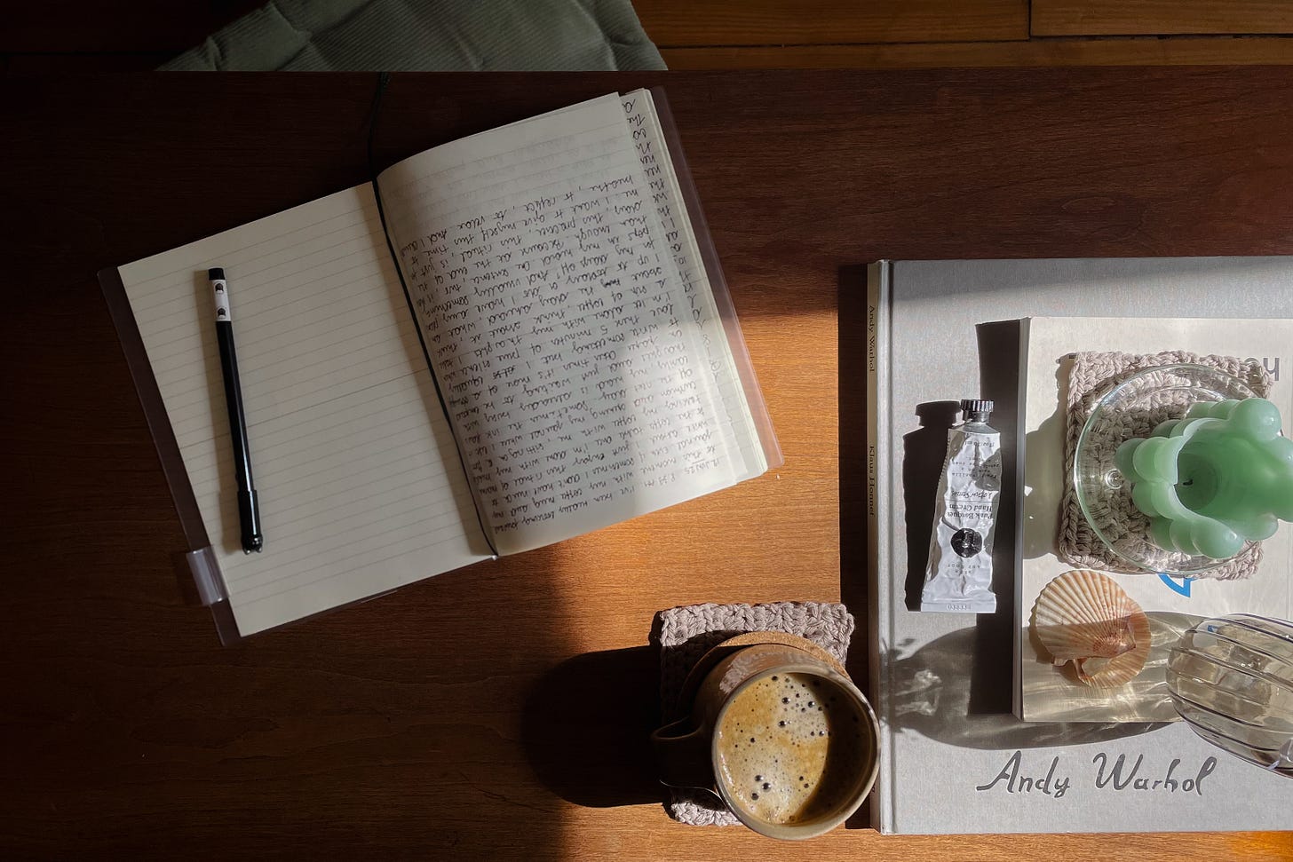 A person sitting at a kitchen table with a notebook and pen, writing reflections about work preferences next to a cup of coffee