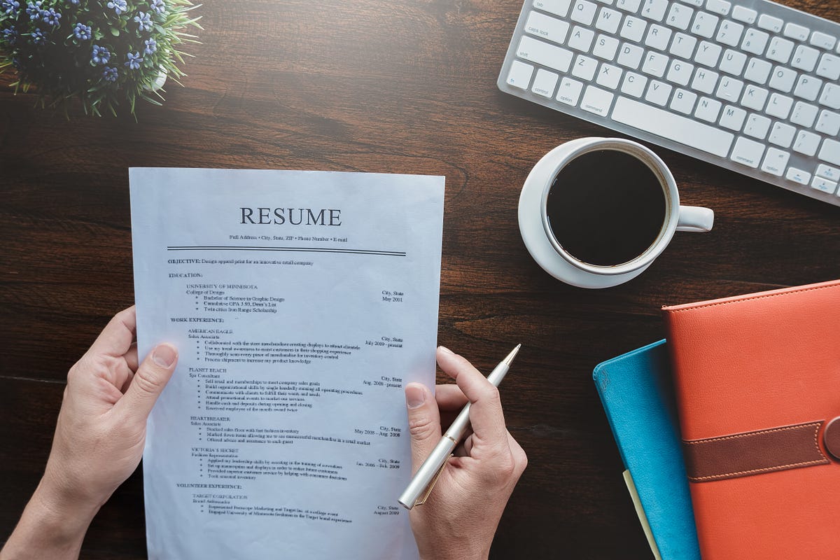 A printed resume laid on a tidy desk next to a notebook and pen, with hands making small edits and notes
