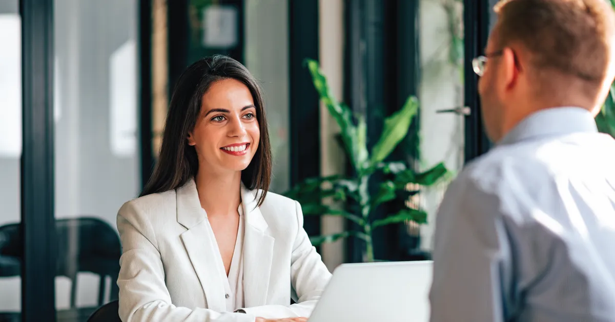 An employee sitting in a small conference room having a professional one-on-one conversation with their manager, both with notebooks on the table