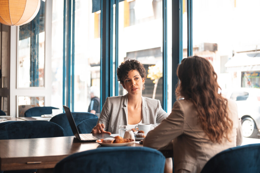Two professionals seated at a coffee shop table having an informational interview conversation with notebooks open